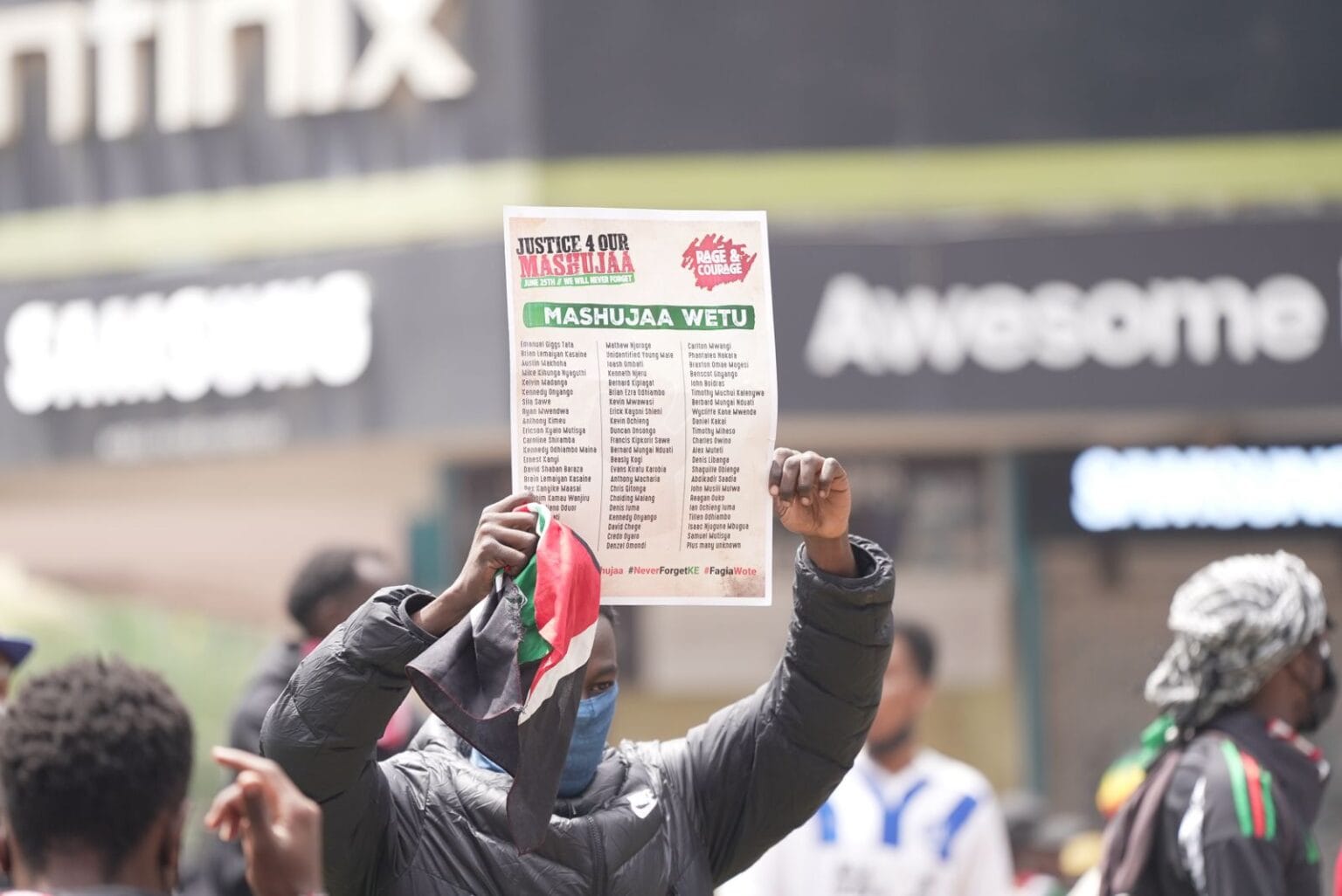A protester holds up a placard listing the names of those killed during the June 25, 2024 demonstrations — a solemn act of remembrance amid the chaos of the 2025 memorial protest in Nairobi.